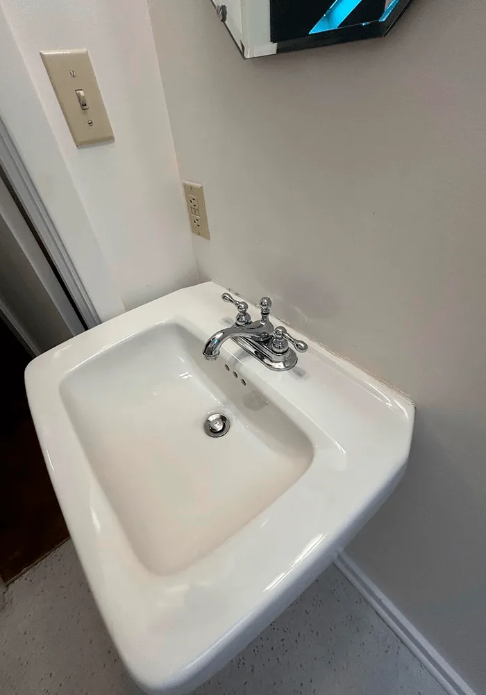 A sparkling clean white pedestal sink with a polished chrome faucet, demonstrating a professional bathroom cleaning service.