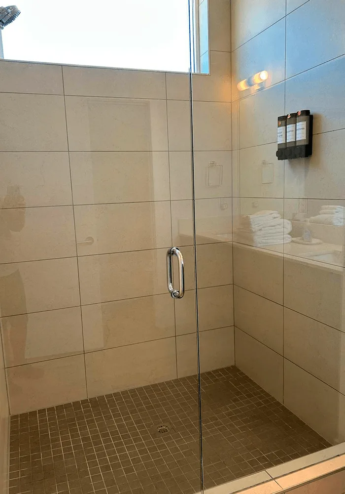 A clean walk-in shower with streak-free glass doors, sanitized tile walls, and a mounted soap dispenser, ready for guest use.