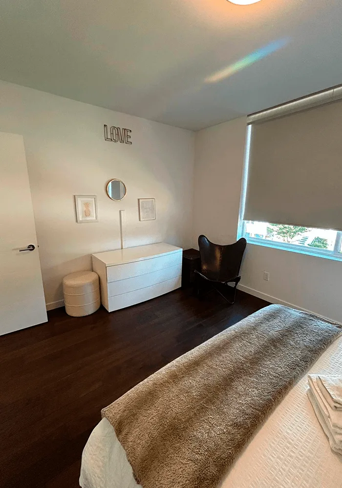 A clean, modern bedroom with dark hardwood floors, a white dresser, and a neatly made bed, showcasing a professional residential cleaning service.