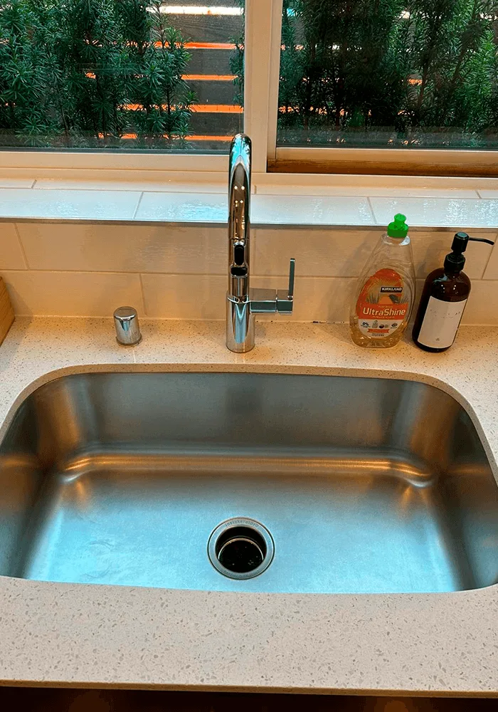 A sparkling clean undermount stainless steel kitchen sink with a polished chrome faucet and clean quartz countertops.