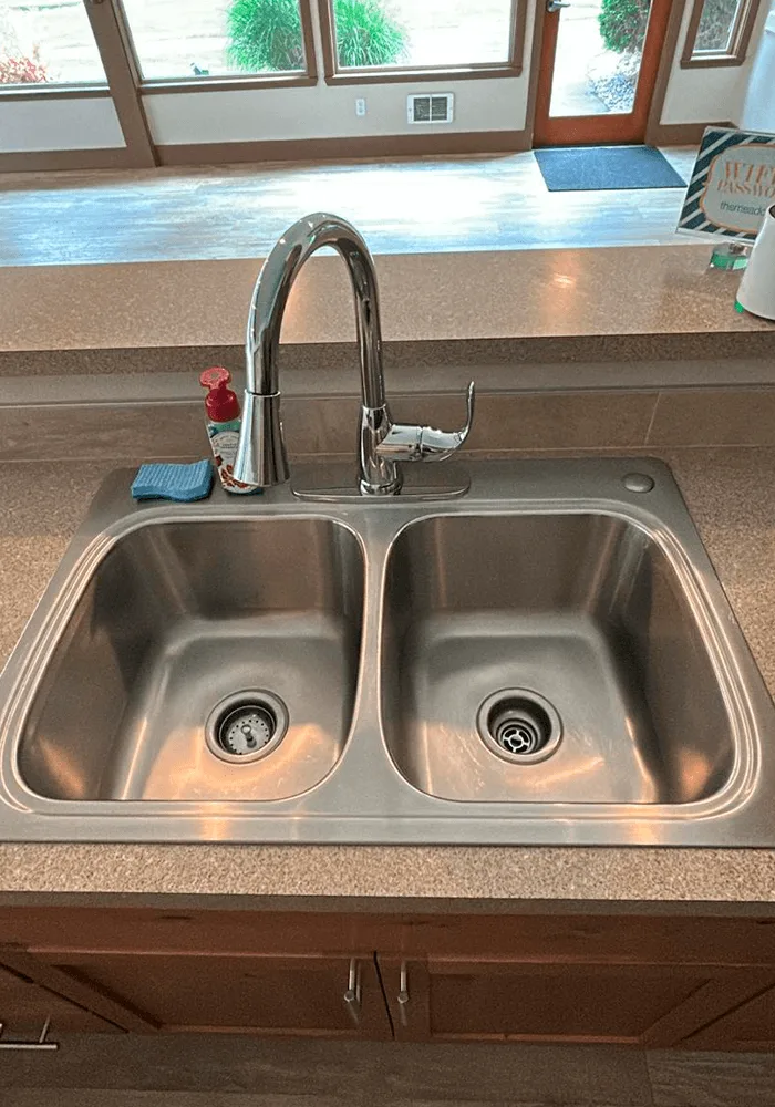 A sparkling clean double-basin stainless steel kitchen sink with a polished high-arc faucet, after a professional cleaning service.