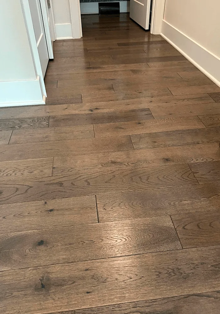 A close-up of gleaming, professionally cleaned hardwood floors in a hallway, showing a flawless, dust-free surface.
