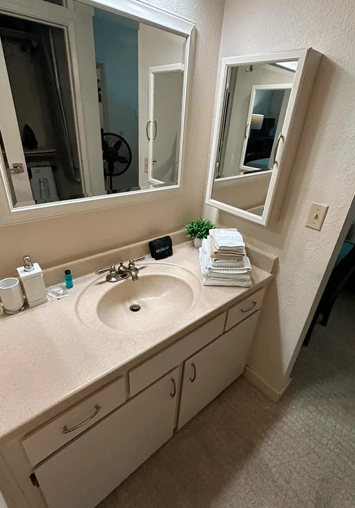 A clean bathroom vanity with a spotless countertop, streak-free mirrors, and a fresh stack of towels, prepared for guests.