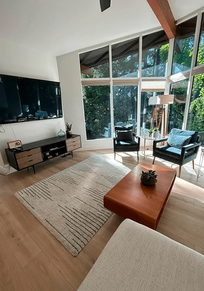 A bright, modern living room with large windows, clean hardwood floors, and a professionally vacuumed area rug, showcasing a premium home cleaning service.