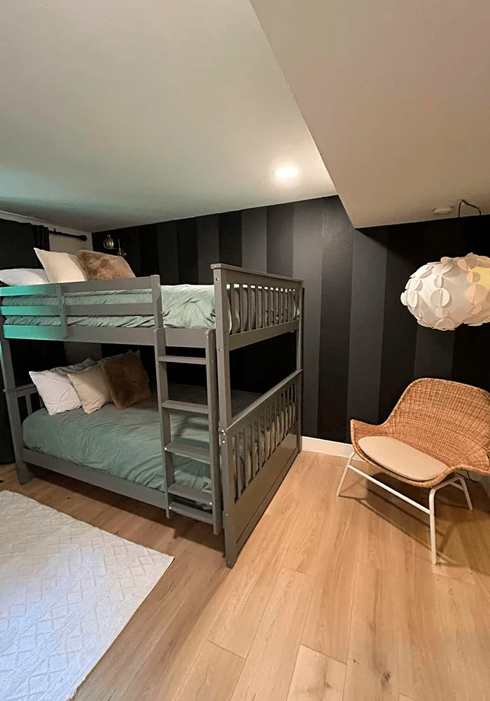 A clean and stylish bedroom with a gray bunk bed, clean laminate floors, and a neatly made bed, perfect for kids or guests.