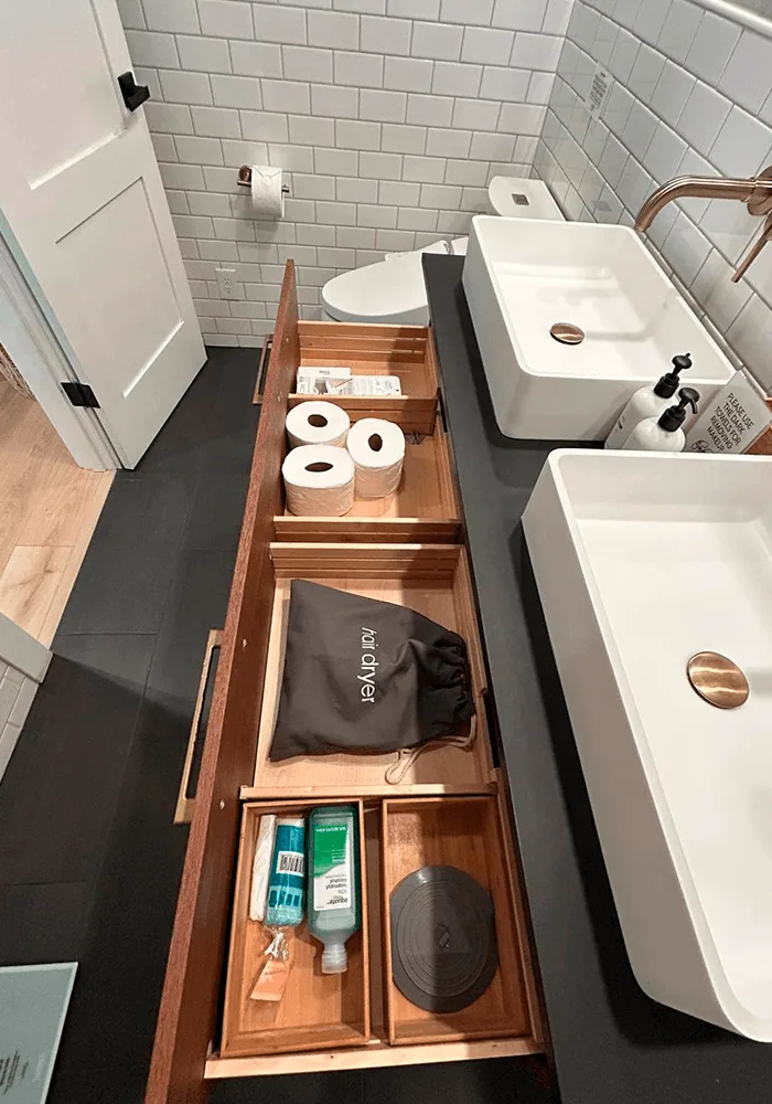 An organized bathroom vanity with open drawers showing neatly arranged toiletries, toilet paper, and a hairdryer, prepared by a professional cleaning service.