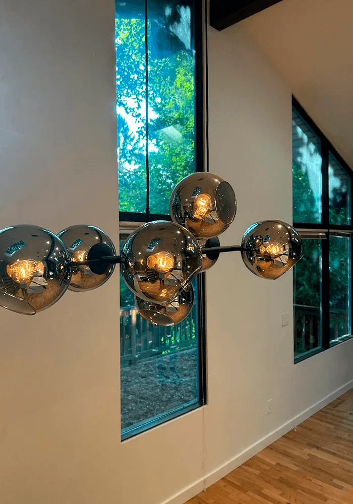 A modern chrome and glass chandelier, sparkling clean and free of dust, hanging in a room with large windows and hardwood floors.