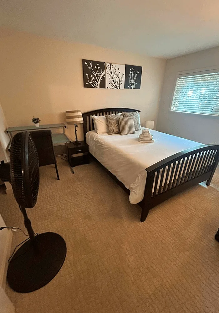 A clean bedroom with freshly vacuumed carpets, a neatly made bed with towels, and dust-free furniture, ready for occupancy.