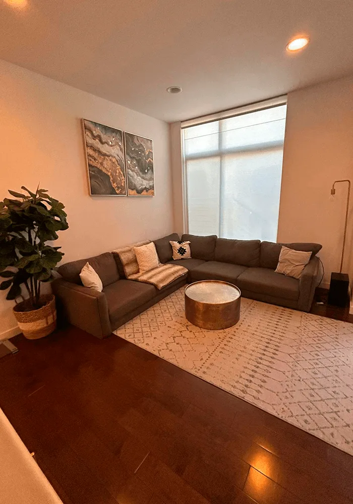 A stylish living room with a large sectional sofa, clean area rug, and polished dark hardwood floors, maintained by a professional home cleaning service.