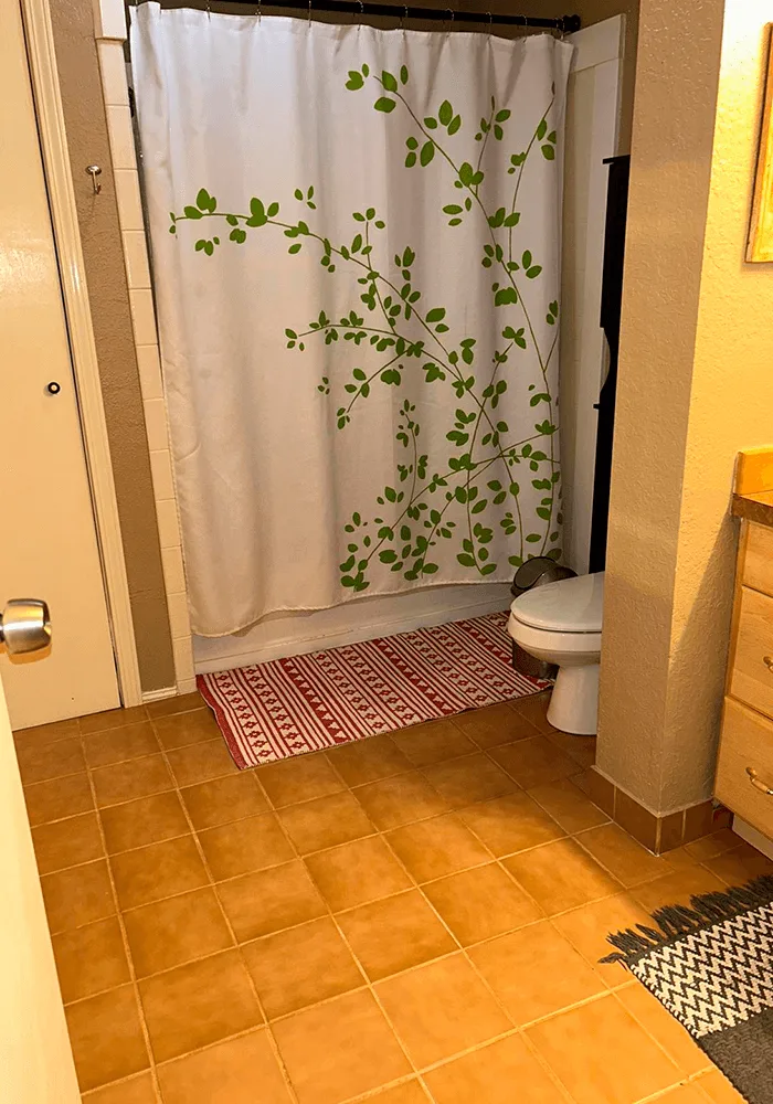 A clean bathroom with terracotta tile floors, a fresh shower curtain, and clean rugs, showcasing a professional tile and grout cleaning service.