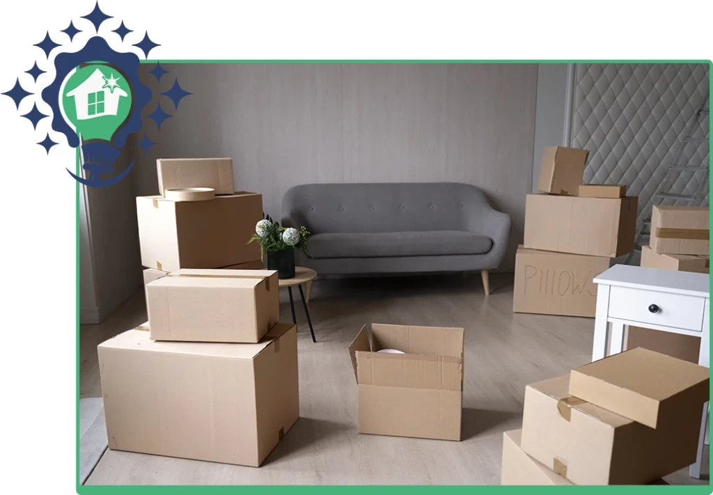 Living room filled with cardboard moving boxes, a gray sofa, and a side table, indicating a home relocation.